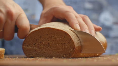 Cut-bread-with-a-knife-on-a-wooden-board-closeup-in-the-kitchen.-shred